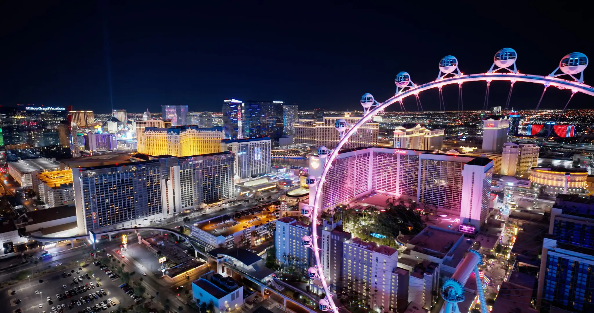 A vibrant cityscape at night featuring a large illuminated Ferris wheel.