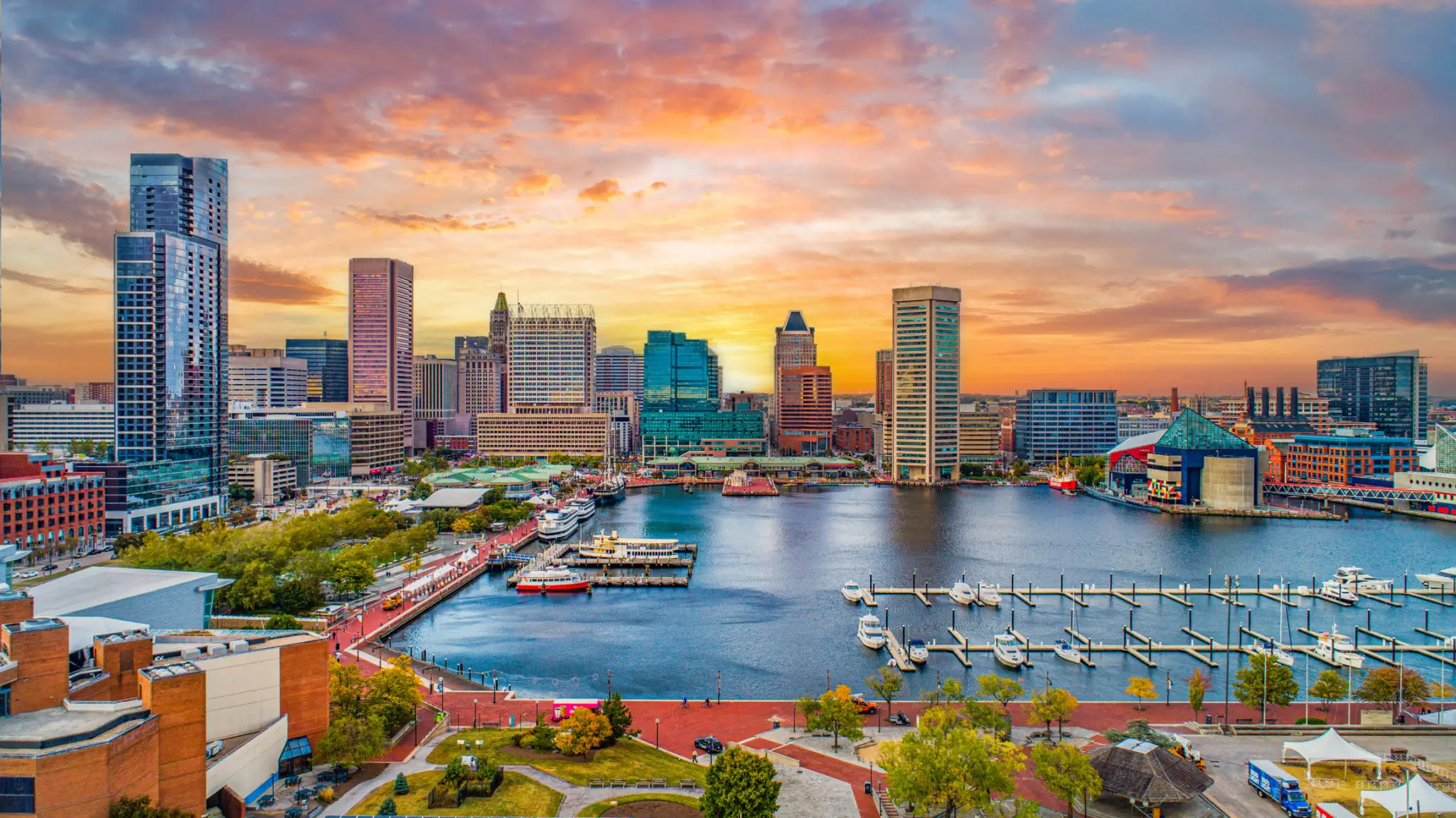 Sunset over a vibrant city skyline with waterfront and boats.