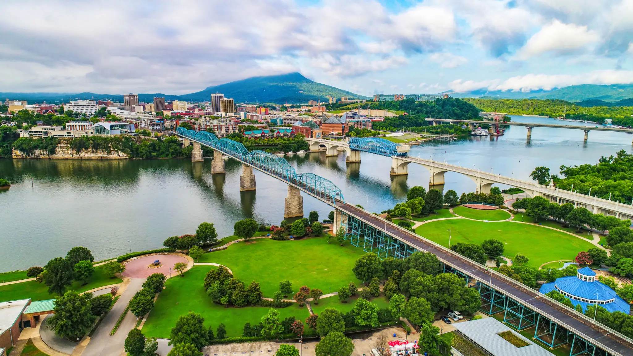 A scenic aerial view of a city with two bridges over a river and a mountain in the background.