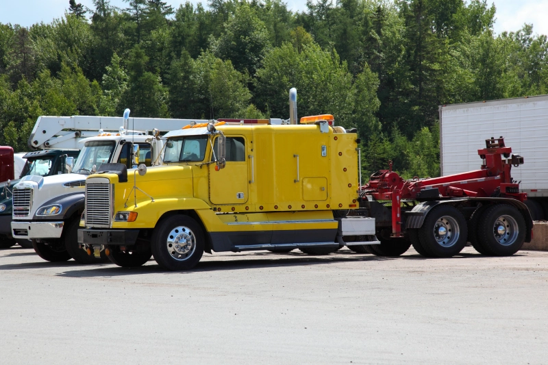 Yellow semi-truck parked with trees in the background.