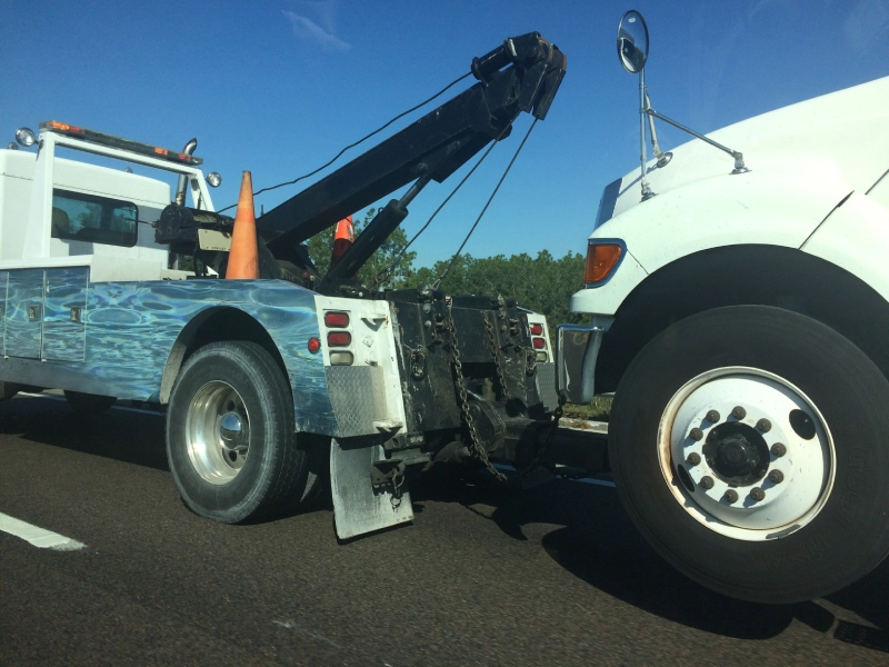 Tow truck hooked to a white truck on the road under a clear sky.